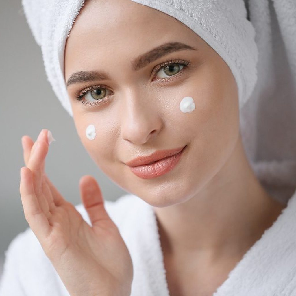 Mujer con toalla y crema facial, sonriendo